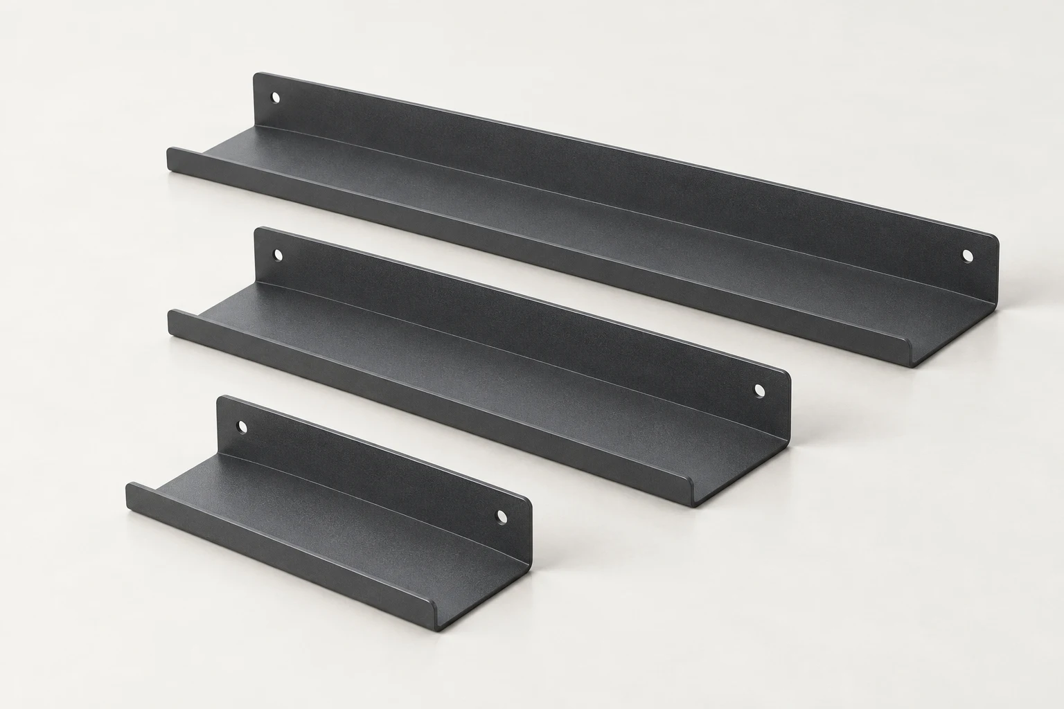 Three graphite folded-steel shelves with drilled back flanges and low front lips, shown in a studio.